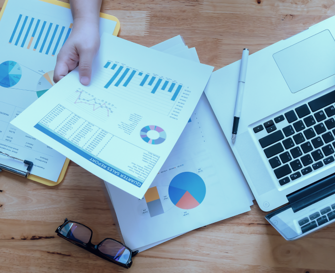 abm campaing example - A hand holding a report with graphs, alongside a laptop, charts, and glasses on a wooden table.