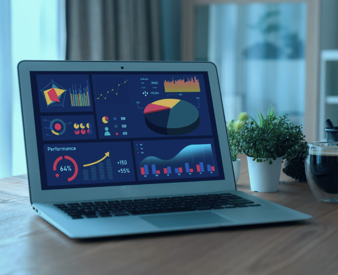 A laptop displays colorful data visualizations, including charts and graphs, on a wooden desk beside a plant and a coffee cup.