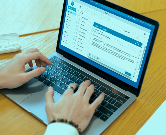A person typing on a laptop with an email marketing dashboard open on the screen, showing a message composition interface. The setting features a wooden table, suggesting a work environment.