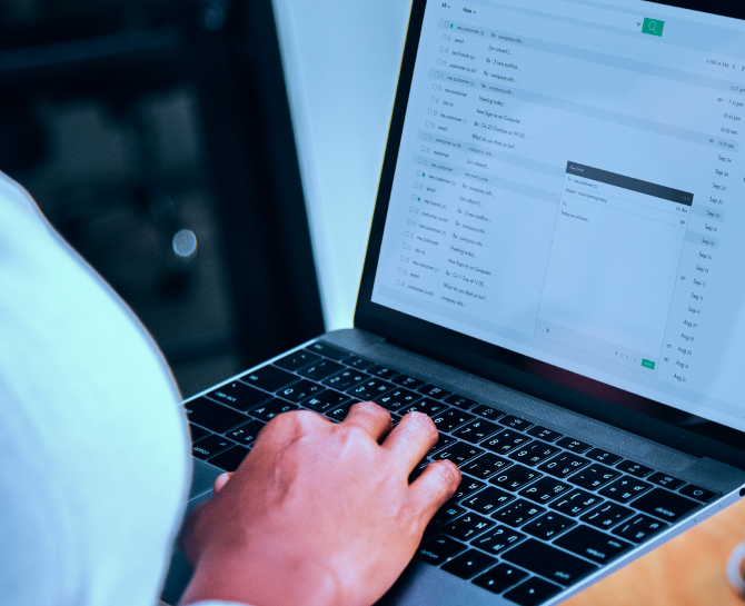 A person uses a laptop displaying an email inbox with several messages. Their hand is on the keyboard, suggesting work or communication.